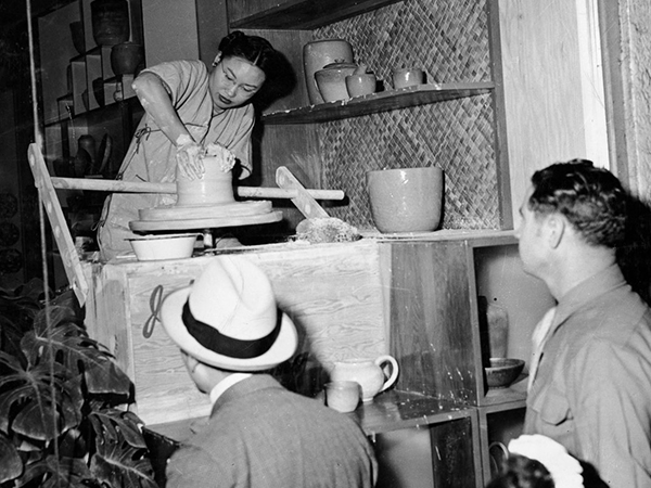 A woman sculpts clay while two men look on.